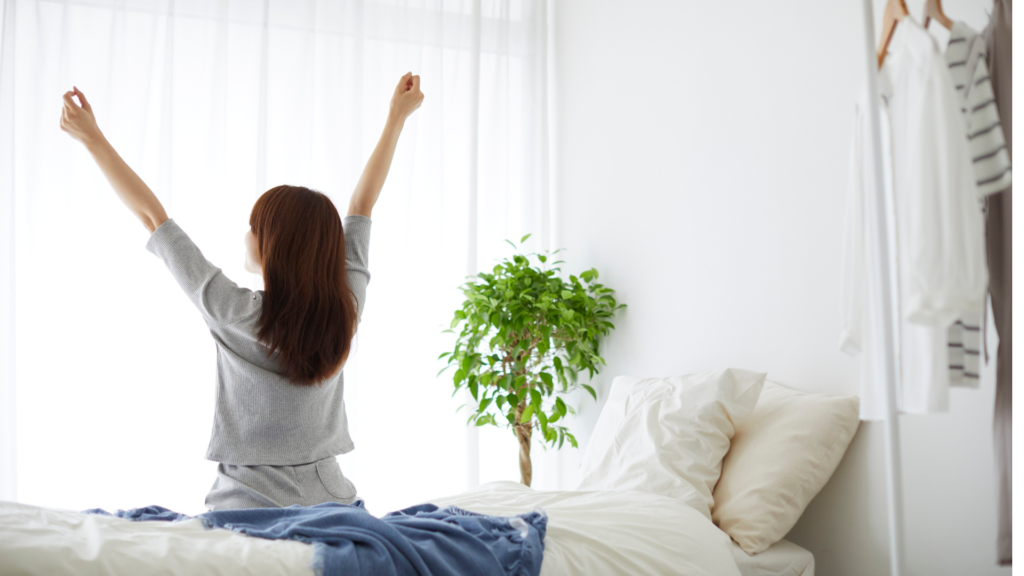 ベッドに座って朝日を浴びる日本人女性の画像