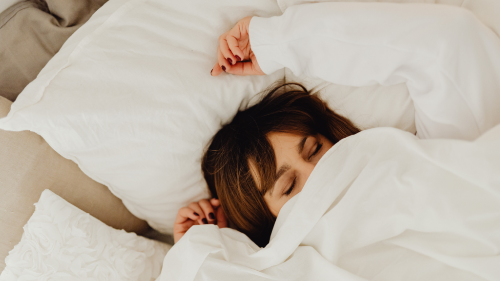 白い毛布にくるまってベッドで気持ちよく眠る女性の画像